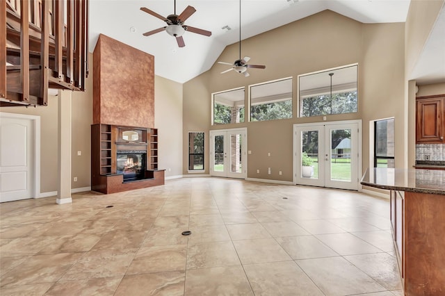 unfurnished living room with light tile patterned flooring, high vaulted ceiling, a fireplace, ceiling fan, and french doors