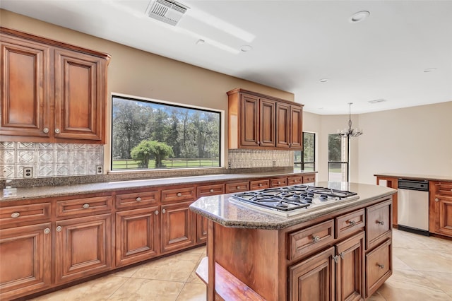 kitchen featuring stainless steel gas cooktop, hanging light fixtures, a kitchen island, a notable chandelier, and decorative backsplash