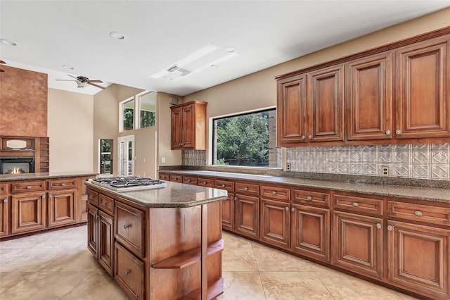 kitchen with dark stone countertops, a large fireplace, a kitchen island, decorative backsplash, and stainless steel gas stovetop