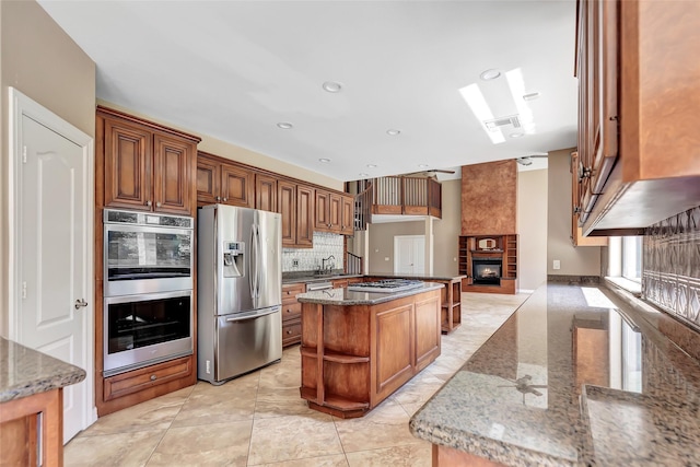 kitchen with a center island, dark stone counters, stainless steel appliances, a fireplace, and decorative backsplash