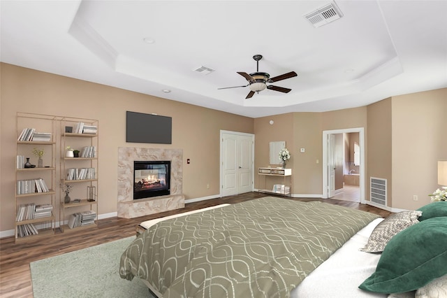 bedroom featuring a raised ceiling, wood-type flooring, connected bathroom, and a fireplace