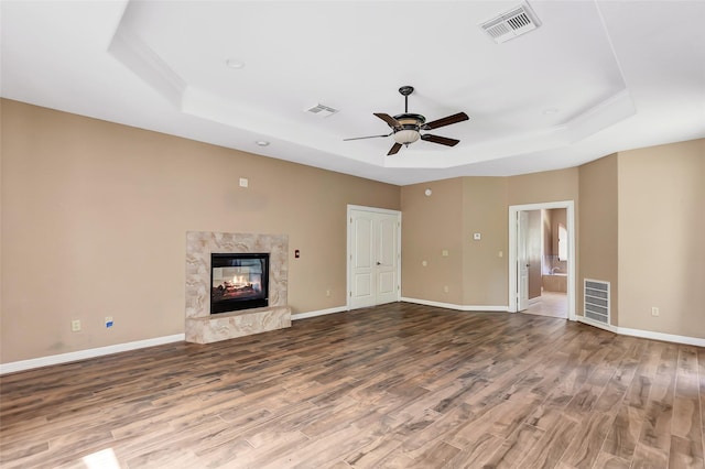 unfurnished living room featuring ceiling fan, wood-type flooring, a fireplace, and a raised ceiling