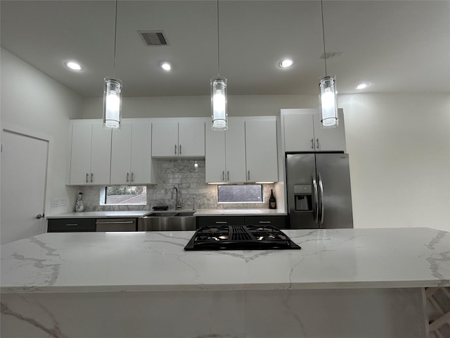 kitchen featuring light stone countertops, appliances with stainless steel finishes, pendant lighting, and a sink