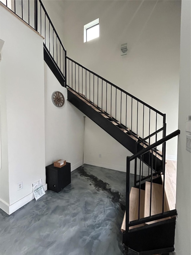 stairway featuring concrete flooring, a towering ceiling, and baseboards