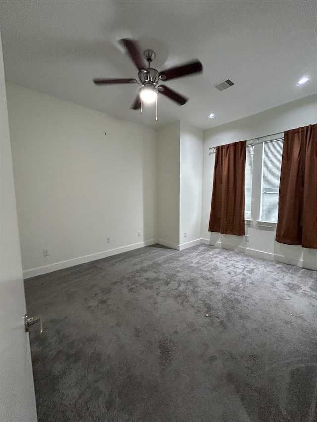 spare room with a ceiling fan, dark carpet, visible vents, and baseboards