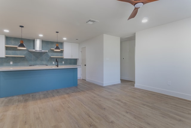 kitchen featuring pendant lighting, tasteful backsplash, white cabinets, light hardwood / wood-style floors, and wall chimney range hood