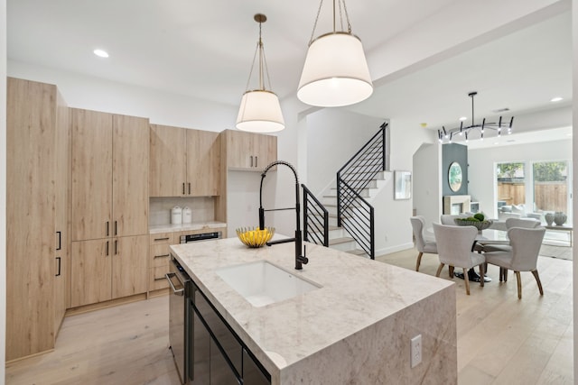 kitchen with a kitchen island with sink, sink, pendant lighting, and light stone counters