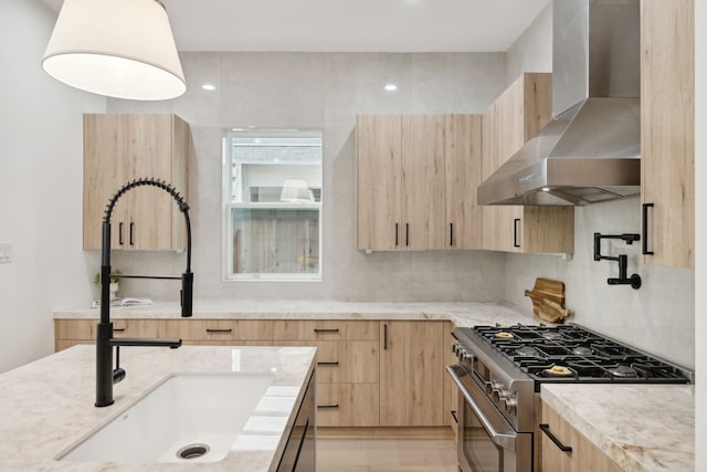 kitchen with stainless steel stove, sink, light stone counters, light brown cabinets, and wall chimney exhaust hood