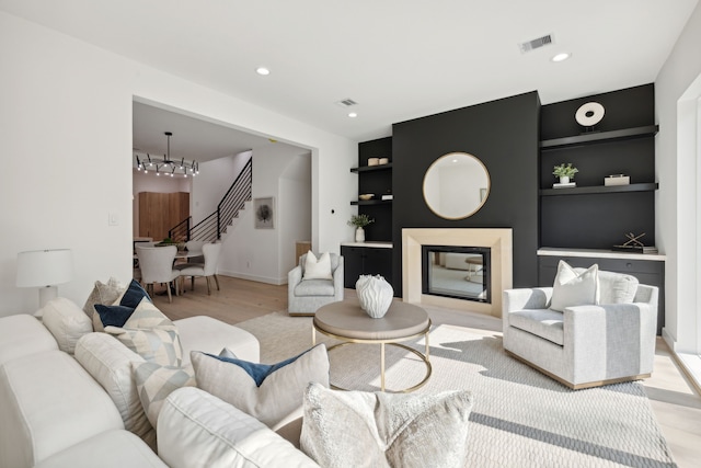 living room with built in shelves, a chandelier, and light hardwood / wood-style floors