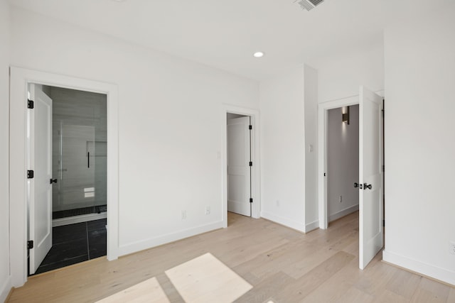 unfurnished bedroom featuring ensuite bath and light hardwood / wood-style floors