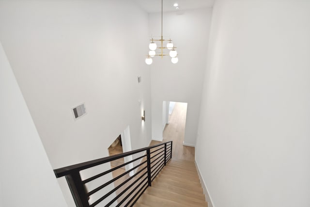 stairs featuring a towering ceiling, hardwood / wood-style floors, and an inviting chandelier