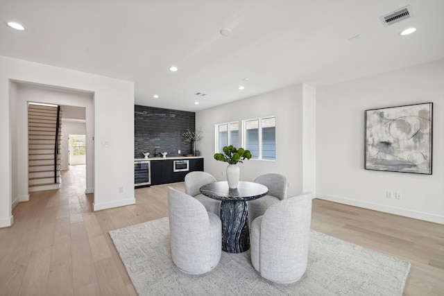 dining space featuring bar, light hardwood / wood-style floors, and beverage cooler