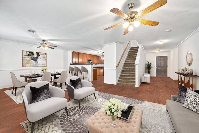 living room featuring ceiling fan, ornamental molding, a textured ceiling, and light wood-type flooring