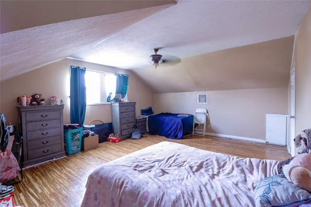 bedroom with ceiling fan, vaulted ceiling, a textured ceiling, and light wood-type flooring