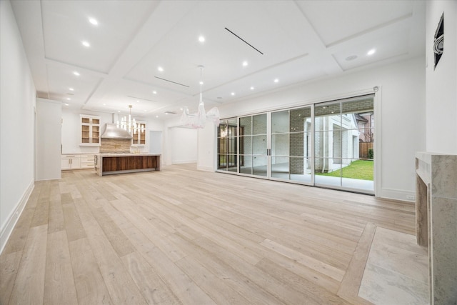 unfurnished living room featuring a premium fireplace, coffered ceiling, an inviting chandelier, and light wood-type flooring