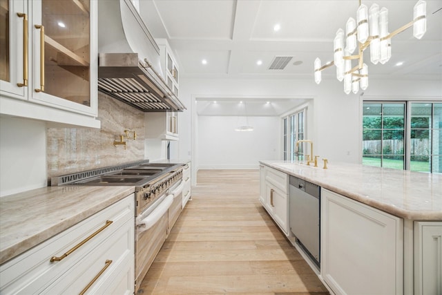 kitchen with white cabinetry, light stone counters, stainless steel dishwasher, and wall chimney exhaust hood