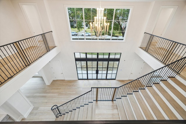 staircase featuring a notable chandelier, wood-type flooring, and a high ceiling