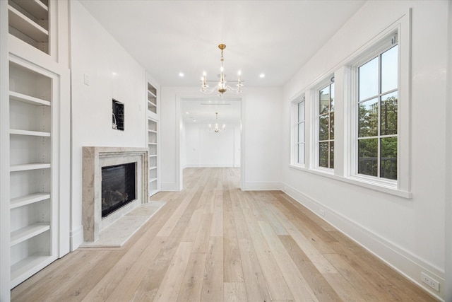 unfurnished living room with light wood-type flooring, a fireplace, an inviting chandelier, and built in shelves