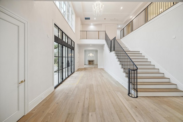 foyer entrance with a towering ceiling, light hardwood / wood-style flooring, and a chandelier