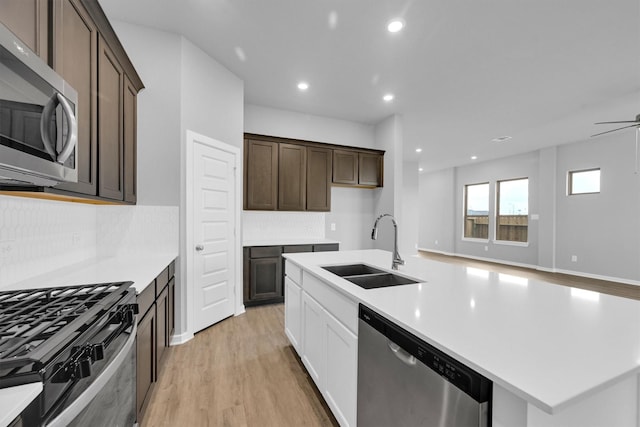 kitchen featuring dark brown cabinets, a center island with sink, light wood-style floors, stainless steel appliances, and a sink