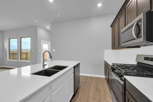 kitchen with light wood finished floors, a sink, light countertops, dark brown cabinetry, and appliances with stainless steel finishes