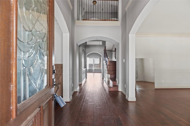 foyer entrance with dark wood-style floors, baseboards, a high ceiling, and arched walkways