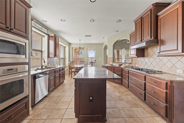 kitchen featuring appliances with stainless steel finishes, a sink, under cabinet range hood, and light stone countertops