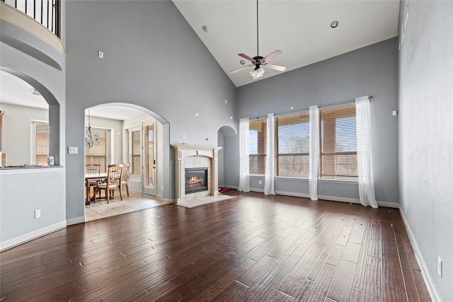 unfurnished living room featuring ceiling fan, arched walkways, wood finished floors, a high end fireplace, and baseboards