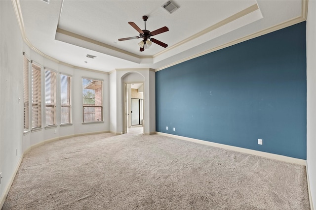 empty room featuring carpet floors, a raised ceiling, visible vents, and crown molding