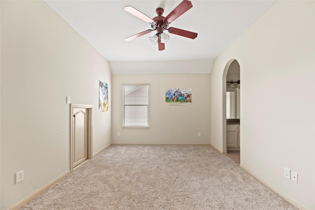 empty room with arched walkways, carpet flooring, vaulted ceiling, ceiling fan, and baseboards