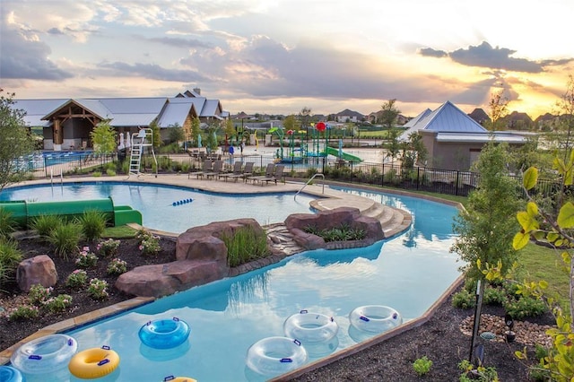 pool at dusk featuring a patio, fence, and a community pool