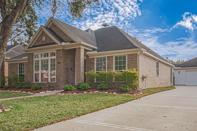 view of front of property featuring a garage, roof with shingles, an outbuilding, a front lawn, and brick siding