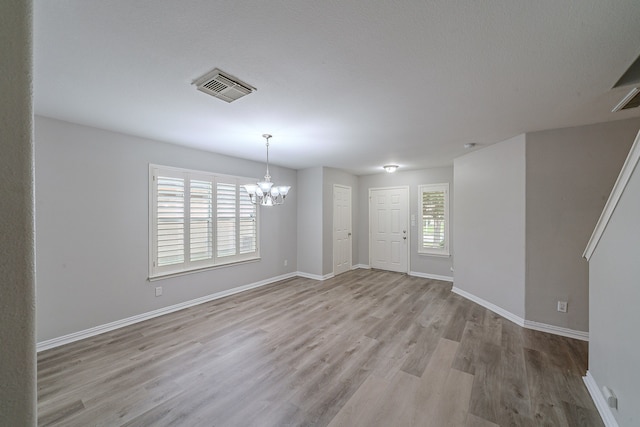 unfurnished dining area with a notable chandelier, a wealth of natural light, and light wood-type flooring