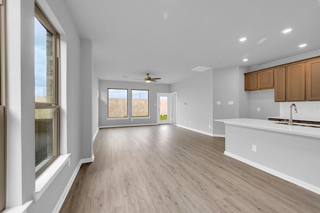 unfurnished living room featuring a ceiling fan, baseboards, recessed lighting, a sink, and light wood-type flooring