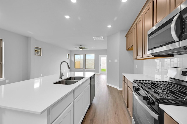 kitchen featuring light wood finished floors, light countertops, decorative backsplash, appliances with stainless steel finishes, and a sink