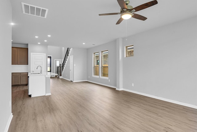 unfurnished living room with visible vents, a sink, light wood finished floors, baseboards, and stairs