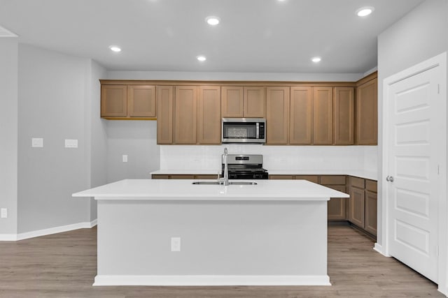 kitchen featuring a center island with sink, recessed lighting, a sink, stainless steel appliances, and light wood-type flooring