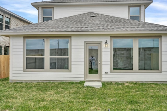 back of house featuring fence, a lawn, and a shingled roof