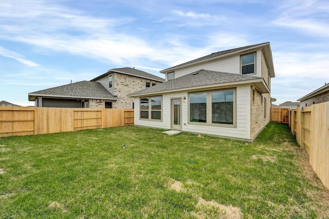 rear view of house with a lawn, roof with shingles, and a fenced backyard