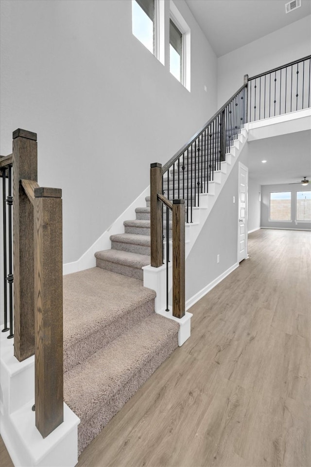 stairway featuring a high ceiling, wood finished floors, visible vents, and baseboards