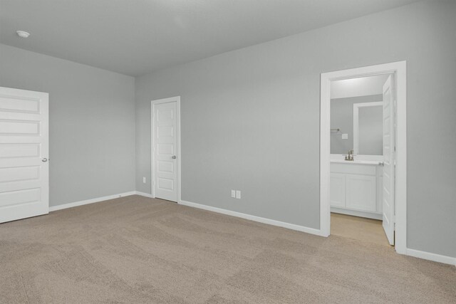 unfurnished bedroom featuring carpet, baseboards, ensuite bathroom, and a sink