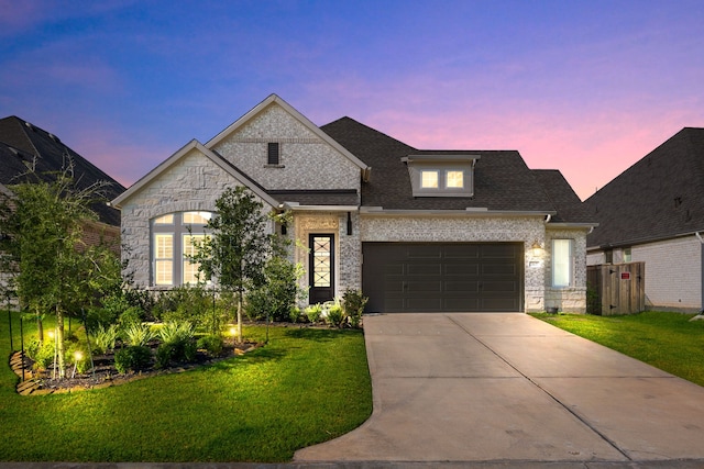 french country home featuring a garage, a shingled roof, brick siding, driveway, and a lawn