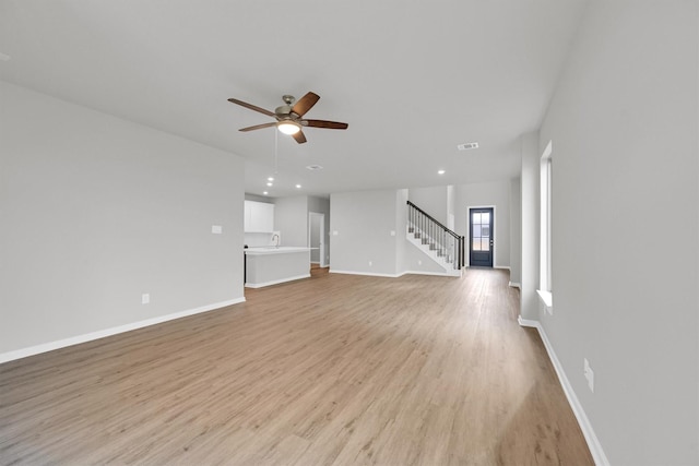 unfurnished living room with stairway, a ceiling fan, visible vents, baseboards, and light wood finished floors