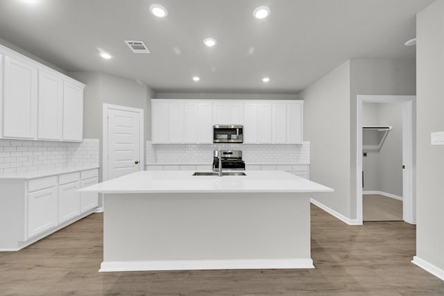 kitchen with light wood finished floors, a kitchen island with sink, appliances with stainless steel finishes, and a sink