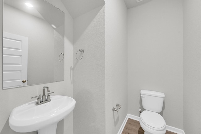 bathroom with toilet, wood finished floors, baseboards, and a sink