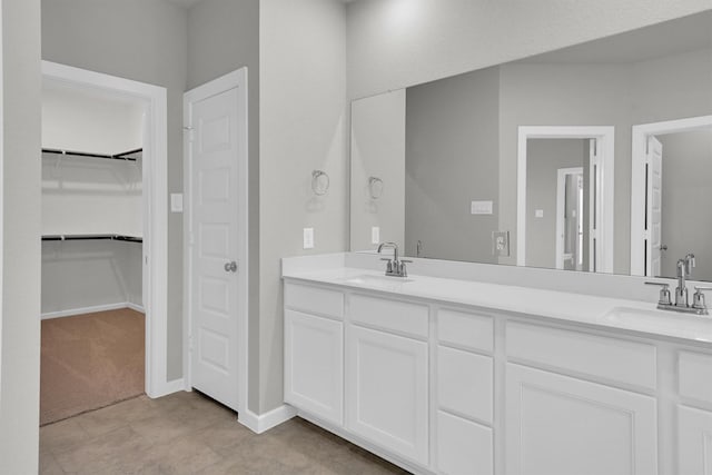 bathroom featuring a walk in closet, double vanity, baseboards, and a sink