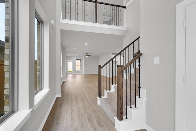 foyer with a ceiling fan, wood finished floors, baseboards, a towering ceiling, and stairs