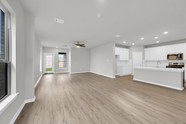 unfurnished living room with visible vents, ceiling fan, baseboards, light wood-style floors, and a sink