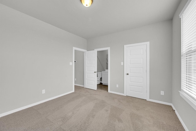 unfurnished bedroom featuring carpet flooring, multiple windows, ensuite bathroom, and baseboards