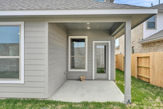 doorway to property featuring a patio area, fence, and roof with shingles